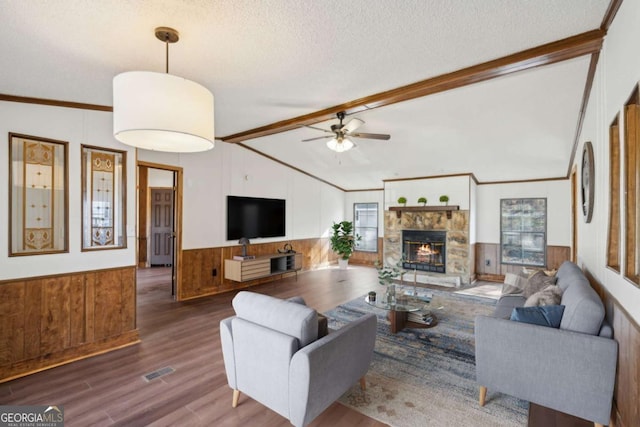 living room featuring a stone fireplace, wooden walls, vaulted ceiling with beams, dark hardwood / wood-style flooring, and a textured ceiling