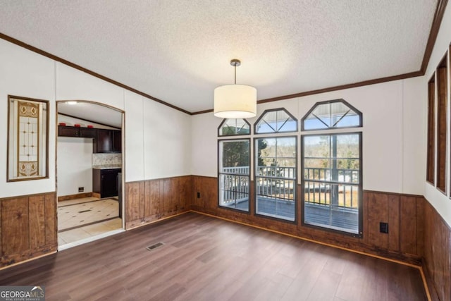 unfurnished dining area featuring wooden walls, ornamental molding, dark hardwood / wood-style floors, and a textured ceiling