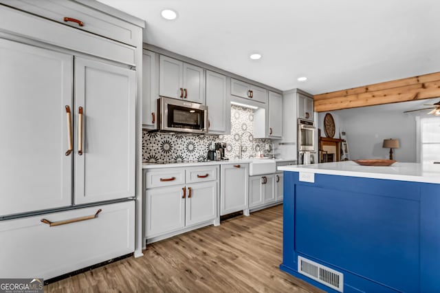 kitchen featuring gray cabinetry, appliances with stainless steel finishes, light hardwood / wood-style floors, and backsplash