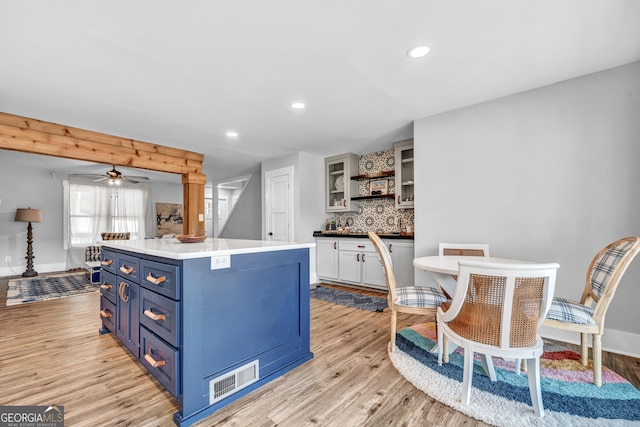 kitchen with light hardwood / wood-style flooring, backsplash, blue cabinets, white cabinets, and a kitchen island