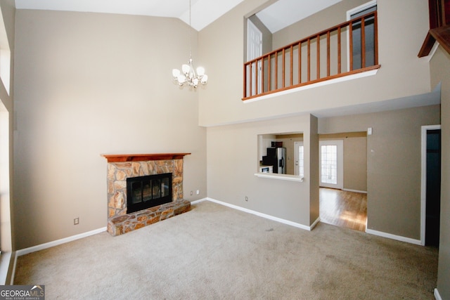 unfurnished living room with an inviting chandelier, carpet flooring, a stone fireplace, and high vaulted ceiling