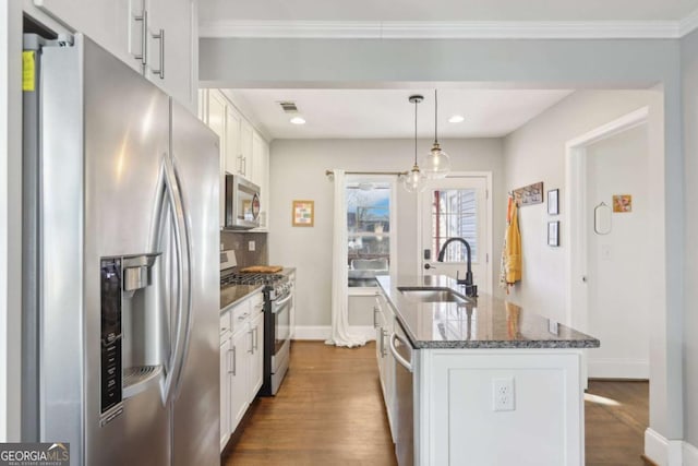 kitchen with appliances with stainless steel finishes, white cabinetry, hanging light fixtures, dark stone countertops, and a center island with sink