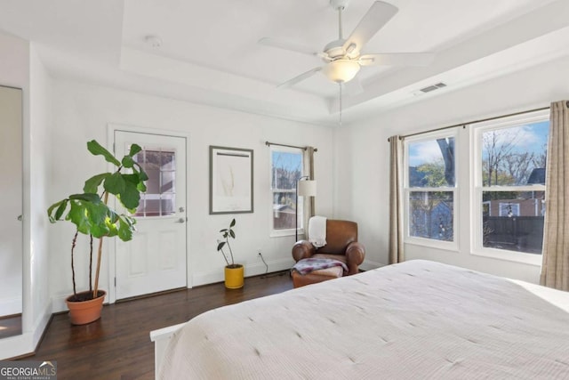 bedroom with dark hardwood / wood-style floors, ceiling fan, and a tray ceiling