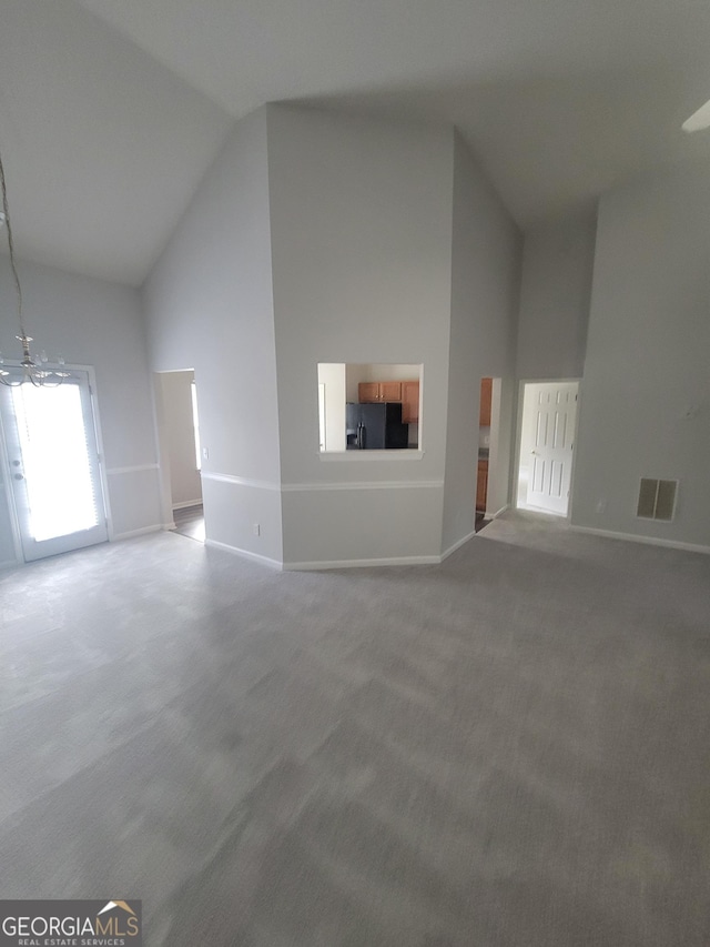 unfurnished living room with a chandelier, high vaulted ceiling, and carpet