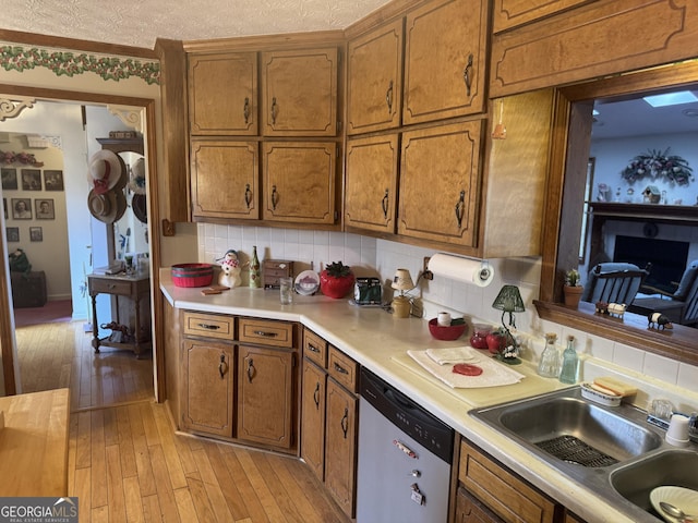 kitchen featuring sink, a textured ceiling, light hardwood / wood-style flooring, stainless steel dishwasher, and backsplash