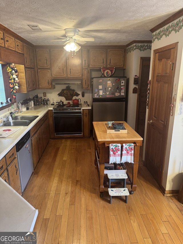 kitchen featuring stainless steel appliances, sink, a textured ceiling, and light wood-type flooring