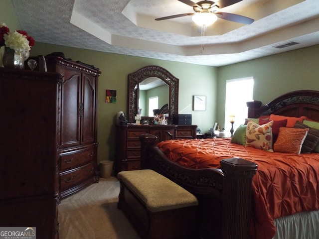 bedroom with a raised ceiling, ceiling fan, light carpet, and a textured ceiling