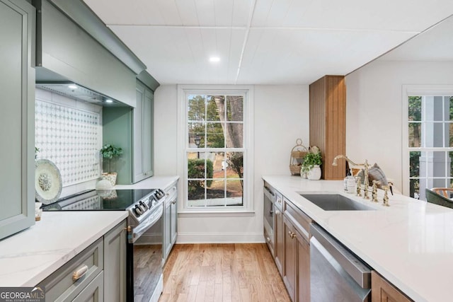 kitchen featuring appliances with stainless steel finishes, sink, light hardwood / wood-style floors, light stone countertops, and wall chimney range hood