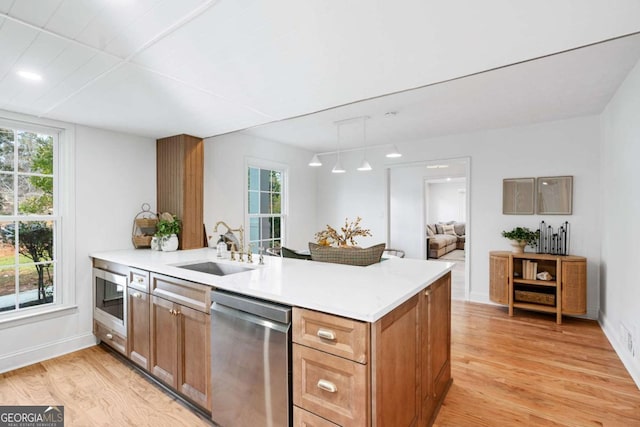 kitchen with sink, hanging light fixtures, kitchen peninsula, stainless steel appliances, and light wood-type flooring