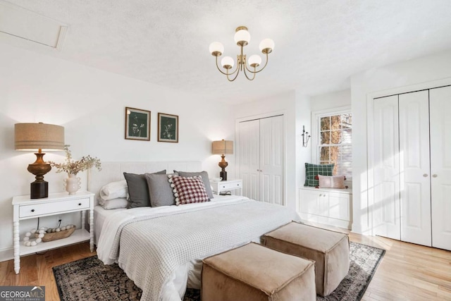 bedroom with two closets, a notable chandelier, a textured ceiling, and light hardwood / wood-style flooring