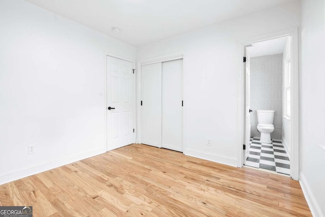 unfurnished bedroom with ensuite bathroom, light wood-type flooring, and a closet