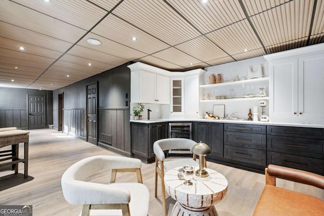 bar with white cabinetry, sink, beverage cooler, and light wood-type flooring