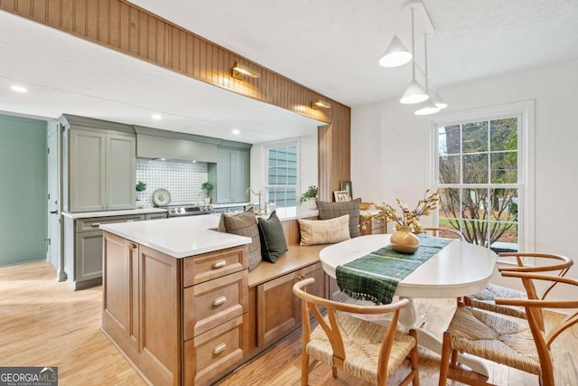 kitchen with a kitchen island, backsplash, hanging light fixtures, light wood-type flooring, and electric stove