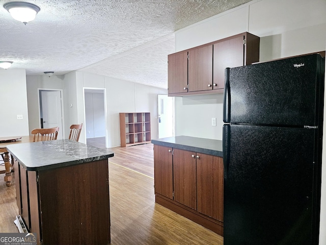 kitchen featuring black refrigerator, a textured ceiling, a kitchen island, vaulted ceiling, and light wood-type flooring