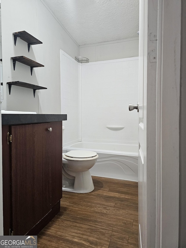 full bathroom with hardwood / wood-style flooring, washtub / shower combination, vanity, a textured ceiling, and toilet