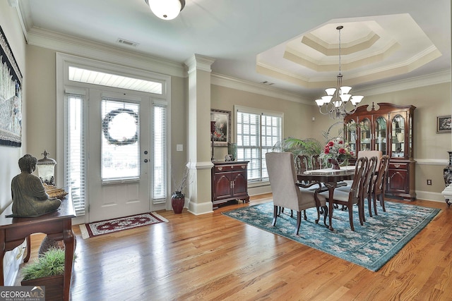 entrance foyer featuring an inviting chandelier, ornamental molding, a tray ceiling, and light hardwood / wood-style floors