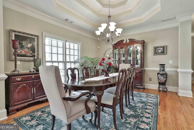 dining room with decorative columns, a tray ceiling, an inviting chandelier, and light hardwood / wood-style floors