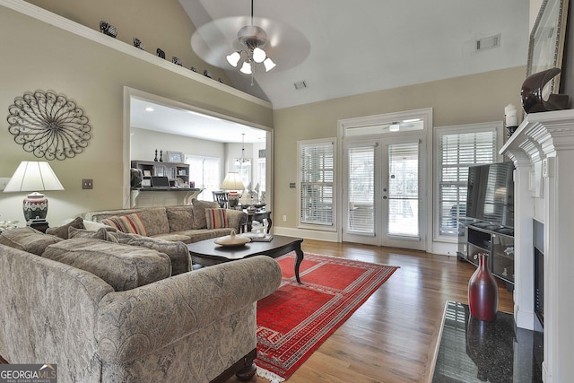 living room with lofted ceiling, hardwood / wood-style flooring, ceiling fan with notable chandelier, and french doors