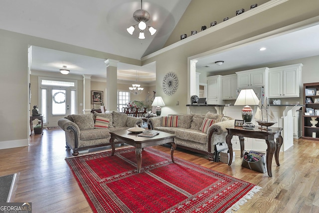 living room featuring light hardwood / wood-style flooring, an inviting chandelier, high vaulted ceiling, ornamental molding, and ornate columns