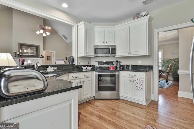 kitchen with sink, stainless steel appliances, white cabinets, dark stone counters, and light wood-type flooring