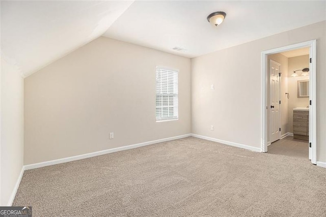 unfurnished bedroom with light colored carpet, lofted ceiling, and ensuite bathroom