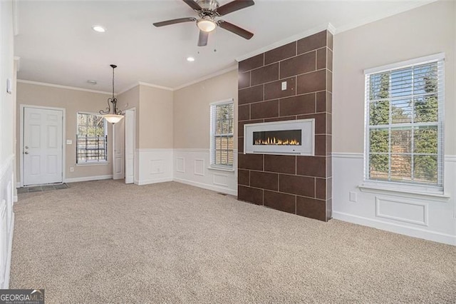 unfurnished living room featuring a tile fireplace, ornamental molding, carpet floors, and ceiling fan