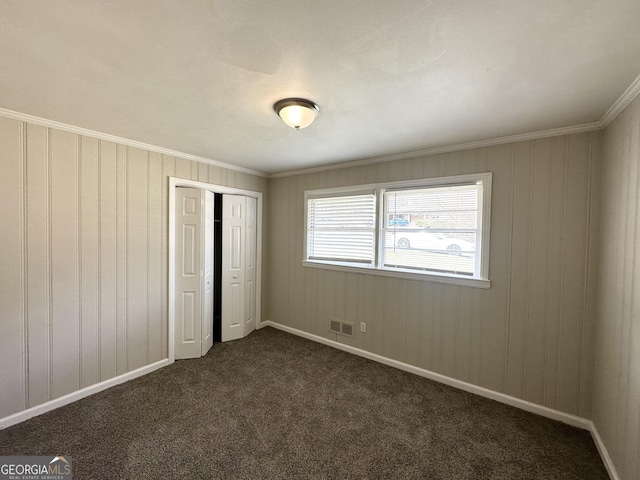 unfurnished bedroom with dark colored carpet, crown molding, and a closet