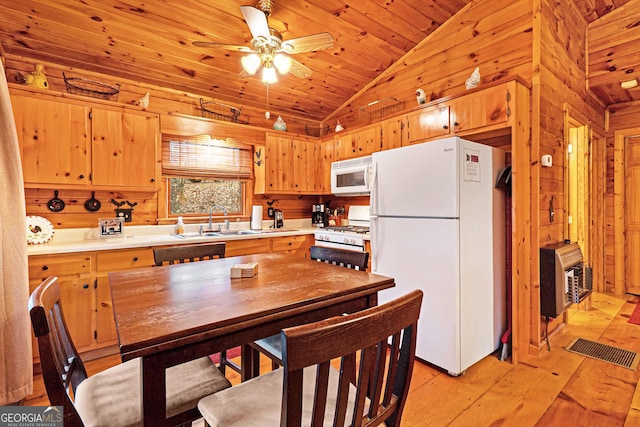 kitchen featuring white appliances, wooden walls, visible vents, vaulted ceiling, and a sink