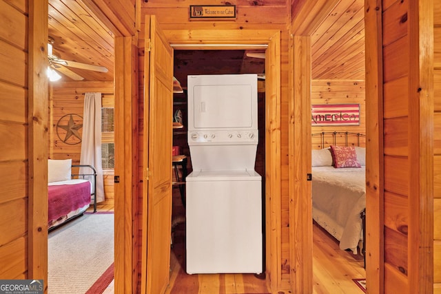 laundry area featuring ceiling fan, laundry area, wood walls, wood finished floors, and stacked washing maching and dryer