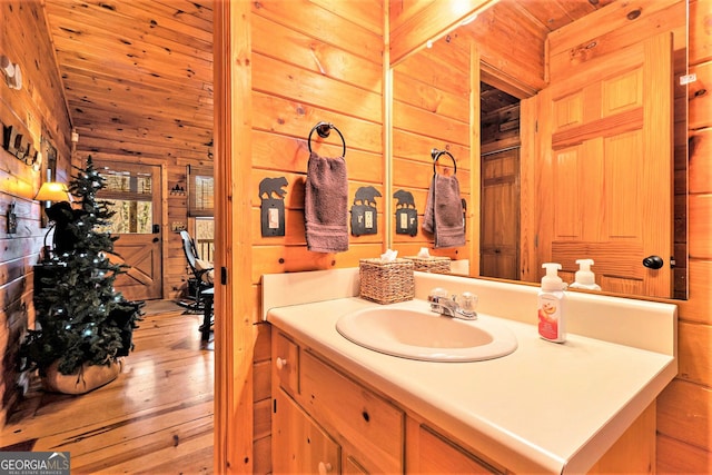 bathroom with lofted ceiling, wooden walls, vanity, wood ceiling, and hardwood / wood-style floors