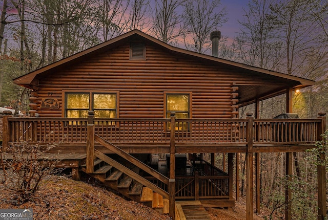 back of house at dusk with stairway, log exterior, and a wooden deck