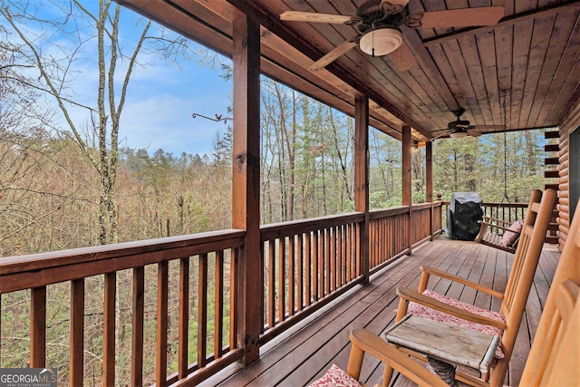 deck with grilling area, a wooded view, and a ceiling fan