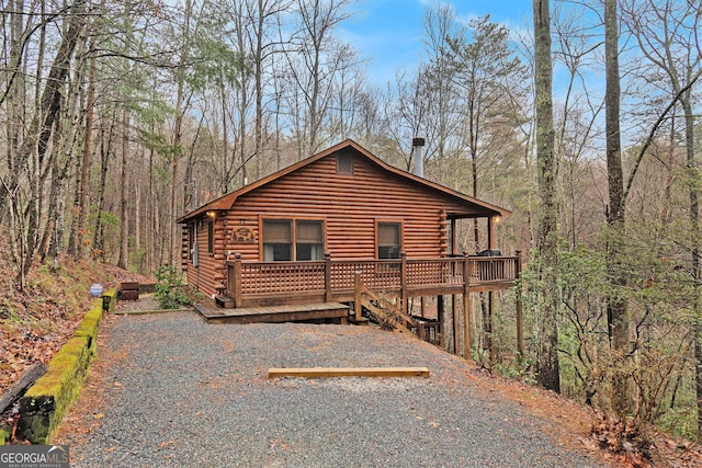 view of front of property featuring log exterior, a wooded view, and a wooden deck