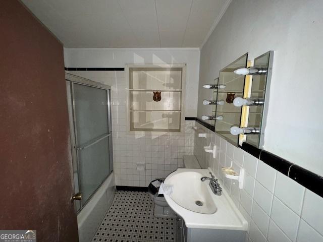 bathroom featuring tile walls, vanity, ornamental molding, and combined bath / shower with glass door