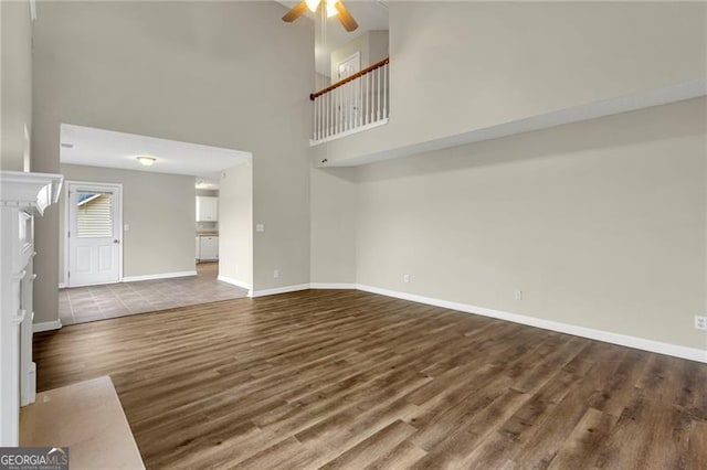 unfurnished living room with hardwood / wood-style floors, a towering ceiling, and ceiling fan