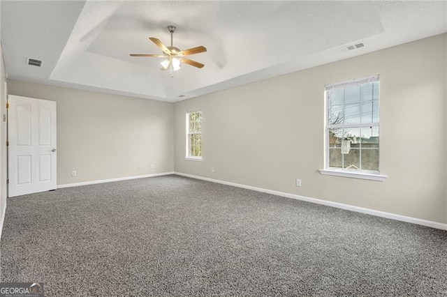 empty room with ceiling fan, a raised ceiling, and carpet floors