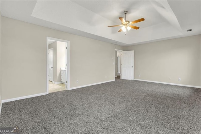 interior space featuring ensuite bathroom, a raised ceiling, and carpet