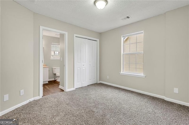 unfurnished bedroom with a closet, carpet flooring, ensuite bath, and a textured ceiling