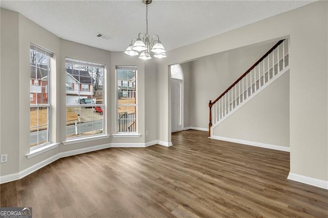 unfurnished dining area featuring dark hardwood / wood-style floors, a chandelier, and a textured ceiling