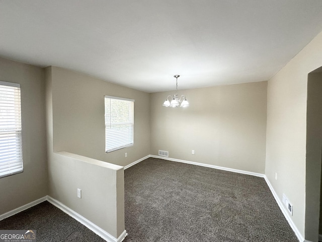 spare room featuring a notable chandelier and dark colored carpet