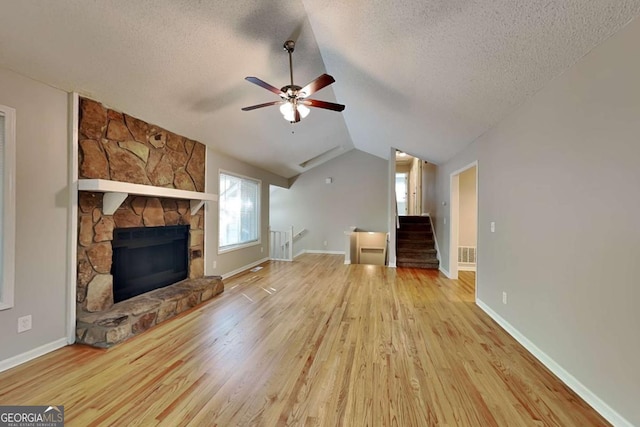 unfurnished living room with lofted ceiling, a stone fireplace, light hardwood / wood-style flooring, and a textured ceiling