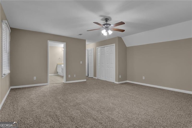 unfurnished bedroom featuring ceiling fan, ensuite bath, light colored carpet, and multiple closets