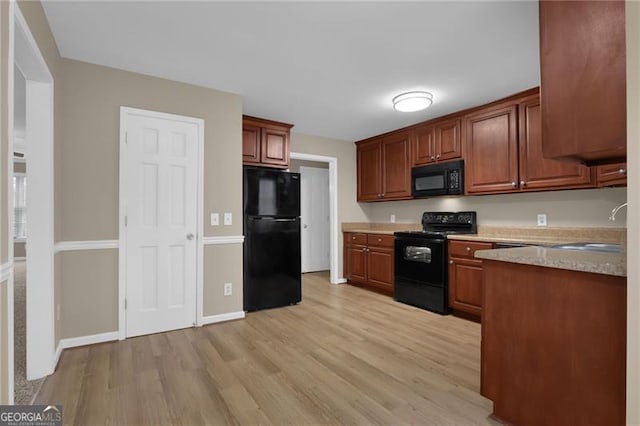 kitchen with light stone counters, light hardwood / wood-style floors, sink, and black appliances