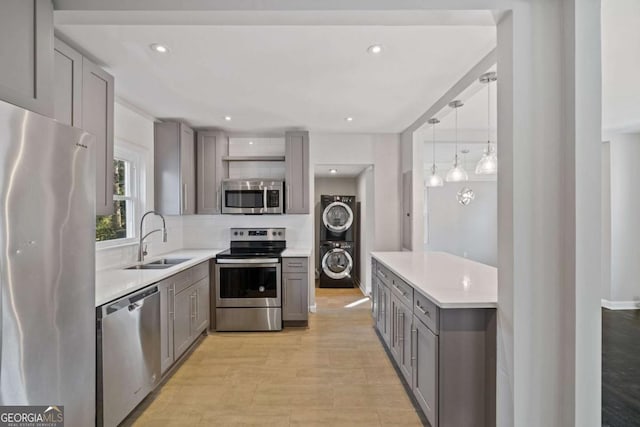 kitchen with sink, gray cabinetry, light wood-type flooring, appliances with stainless steel finishes, and stacked washing maching and dryer