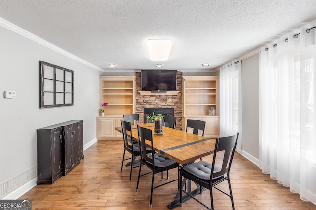 dining space featuring crown molding, a stone fireplace, light hardwood / wood-style floors, and a textured ceiling