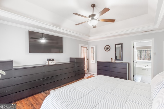 bedroom with connected bathroom, hardwood / wood-style flooring, ornamental molding, ceiling fan, and a tray ceiling