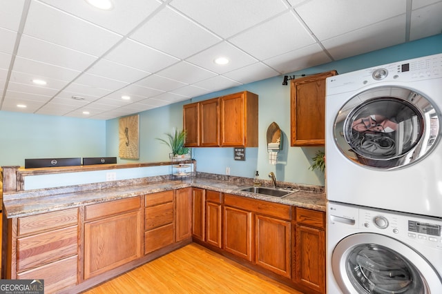 laundry room featuring stacked washing maching and dryer, sink, and light hardwood / wood-style floors