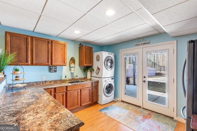 washroom featuring french doors, stacked washer / dryer, sink, and light wood-type flooring