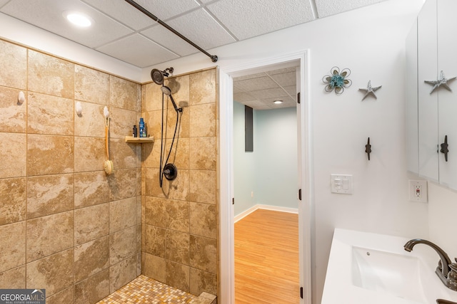 bathroom featuring a paneled ceiling, sink, hardwood / wood-style floors, and a tile shower