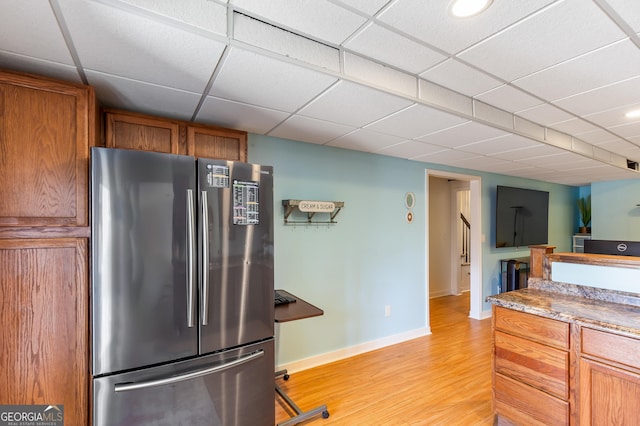 kitchen with a paneled ceiling, light hardwood / wood-style floors, stainless steel refrigerator, and stone countertops